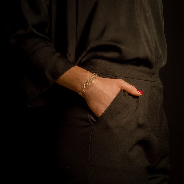 Silhouette féminine habillée en noire avec une main dans la poche de pantalon droite. Le poignet porte un bracelet de la marque Marie Archambaud, bijou unique conçu à la main par une technique de maille au fil de cuivre vernis à l'or.