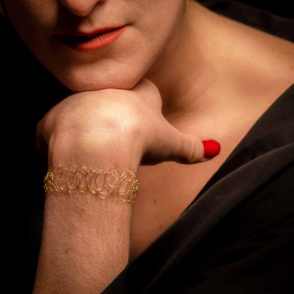Menton posé sur une main portant un bracelet signé Marie Archambaud, marque de bijoux brodés uniques. Ici, c'est le bracelet Lumio en or jaune.