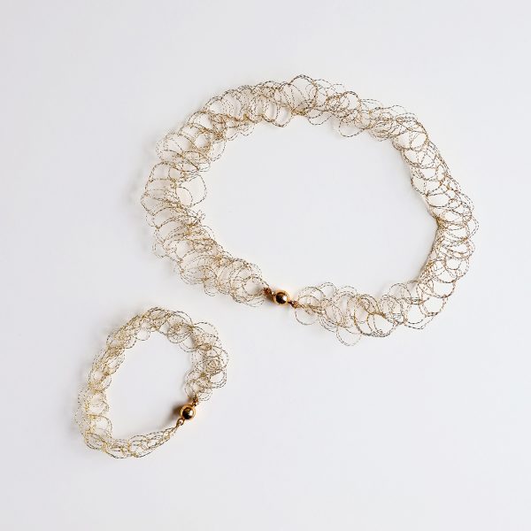 Collier et bracelet au fil doré sur fond blanc faisant ressortir les détails de la maille.