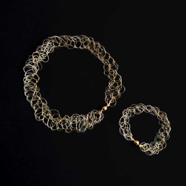 Collier et bracelet au fil doré sur fond noir faisant ressortir les détails de la maille.